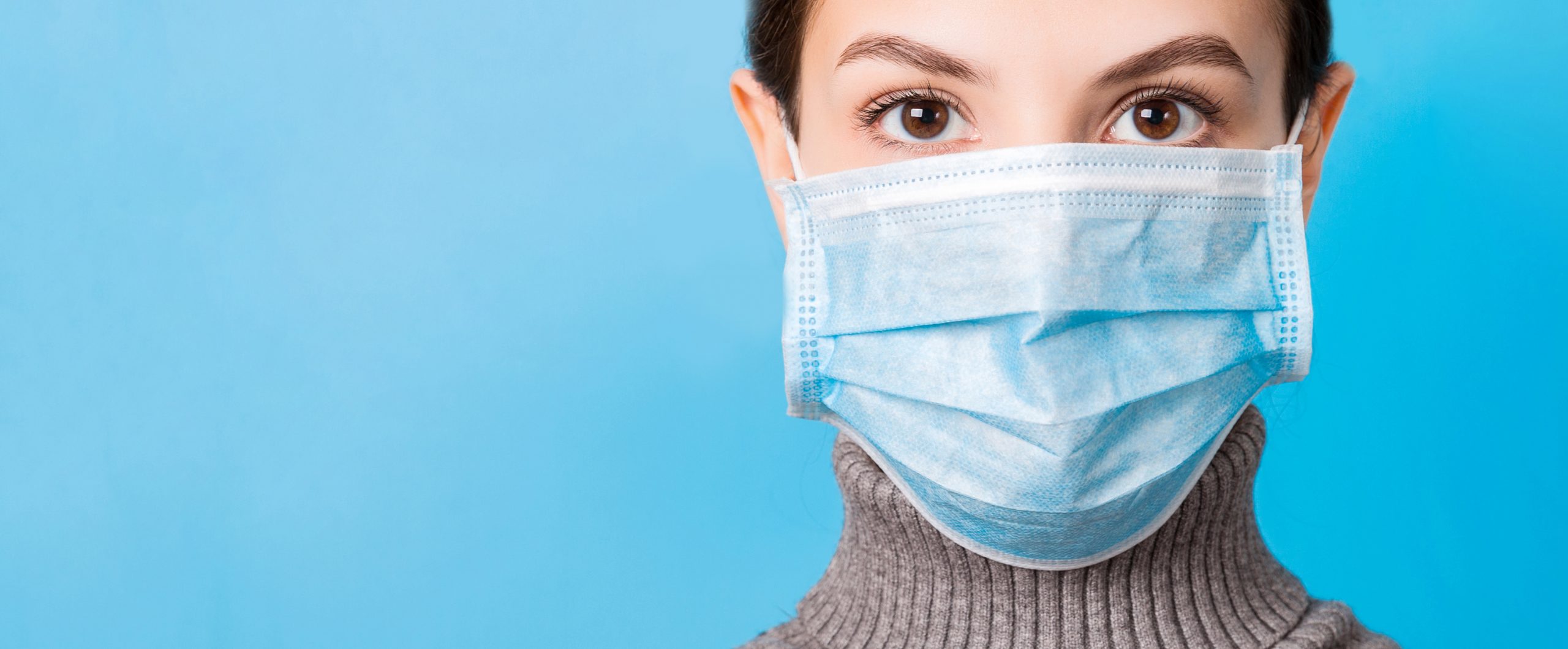 Portrait of young woman wearing medical mask at blue background
