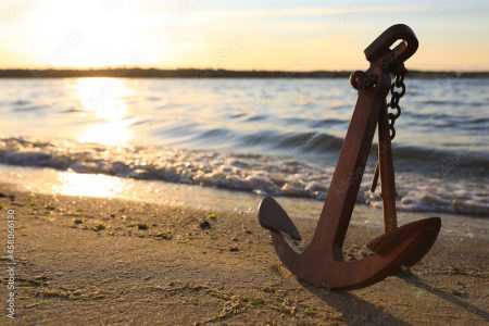 Wooden anchor on shore near river at sunset