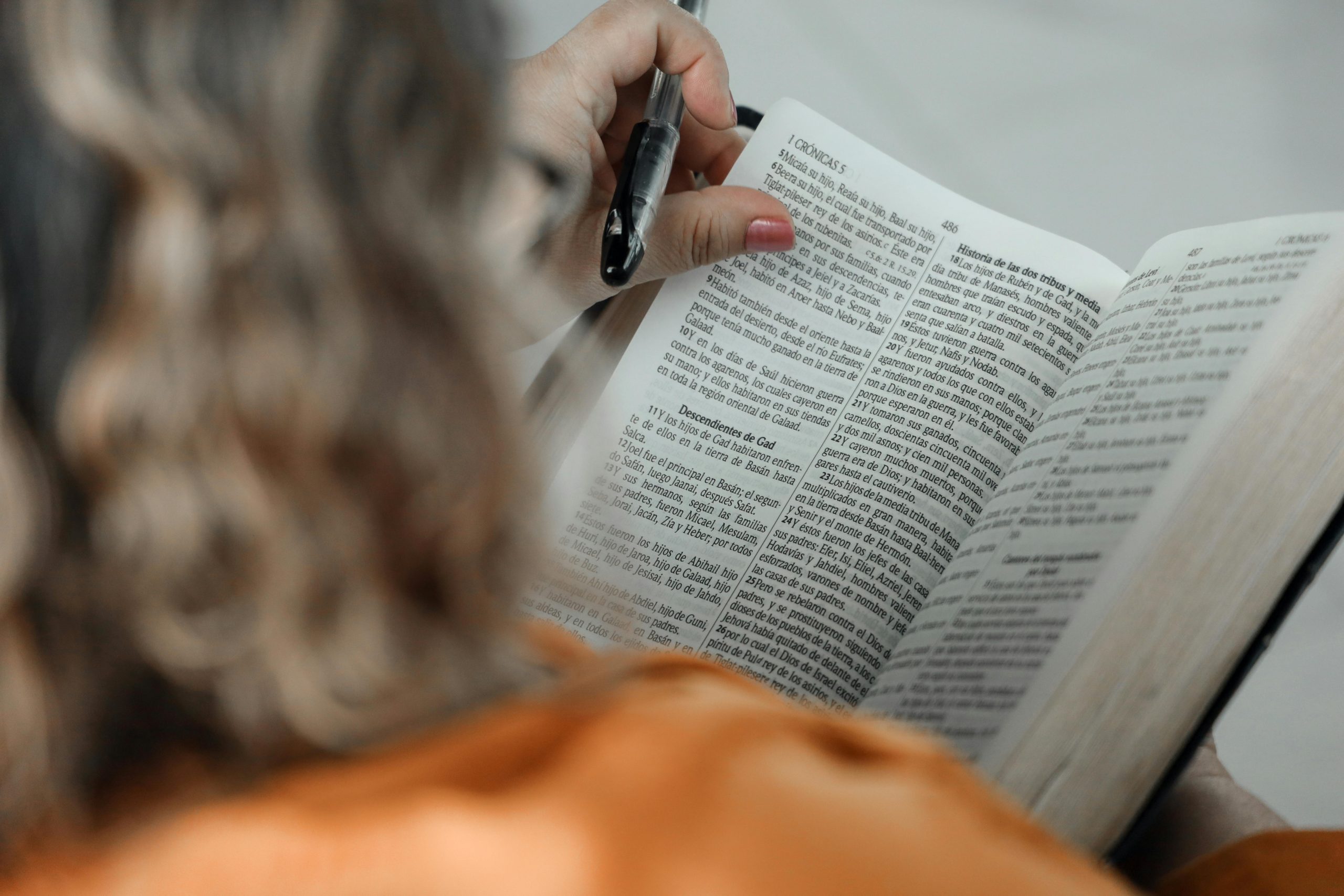 Close-up of a woman reading a Bible with a pen, focused on text.