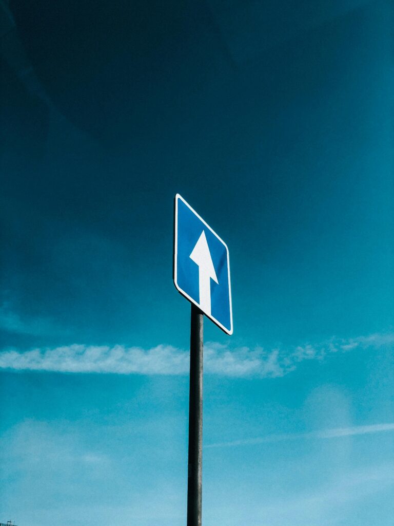 A blue traffic sign with an upward arrow against a clear blue sky, symbolizing direction and movement.